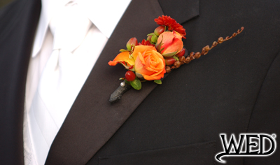 groom's wedding tuxedo lapel with floral boutonniere pinned on it and Wedding Entertainment Director® logo