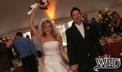 wedding reception bride holding her bouquet up high and groom smiling as they make their grand entrance and Wedding Entertainment Director® logo